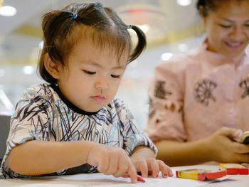 Cute baby girl coloring paper at table in restaurant