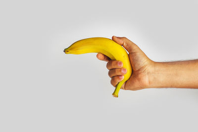 Close-up of hand holding banana against white background