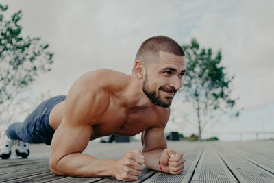 Shirtless young man exercising on footpath