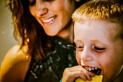 Smiling boy eating chocolate sitting with mother