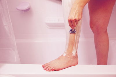 Low section of young woman shaving leg in bathroom