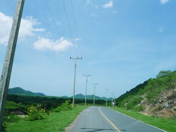 Road by electricity pylon against sky