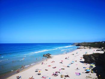 Group of people on beach against clear blue sky