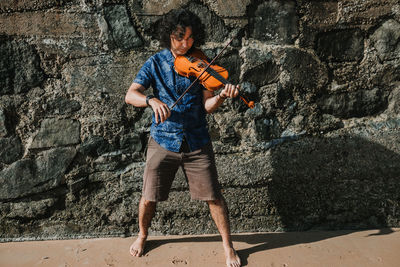 Full length of young man holding umbrella against wall