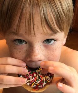 Close-up portrait of shirtless boy eating donut at home