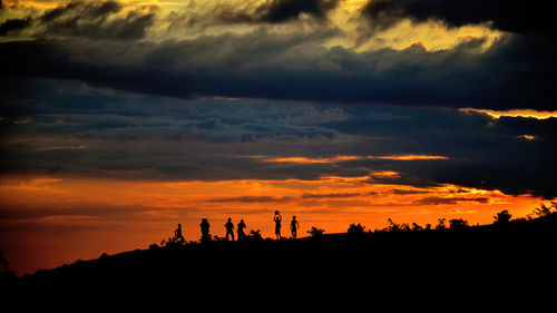 Silhouette people playing on landscape against dramatic sky during sunset