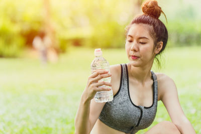 Young woman holding bottle while standing outdoors