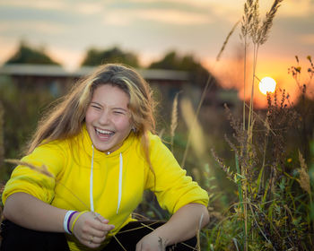 A young girl laughs in a meadow with tall grass in the rays of the setting sun