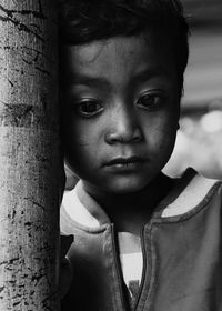 Thoughtful cute boy leaning on tree trunk