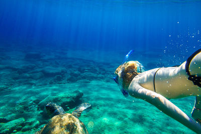 Close-up of mature woman swimming undersea with turtle