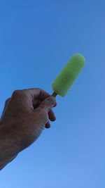 Hand holding ice cream against blue sky