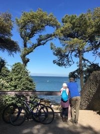 Rear view of old couple cycling on bicycle by plants against sky