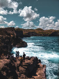 People on rocks by sea against sky