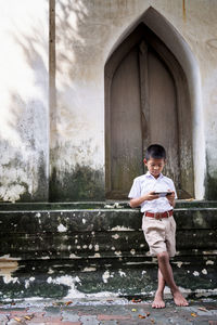 Full length of school boy playing on mobile while standing outdoors