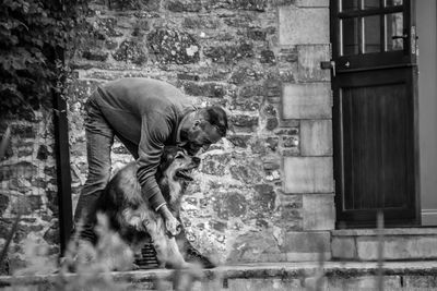 Man with dog bending against wall