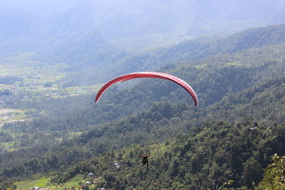 Rear view of man paragliding above green mountains