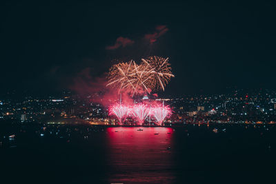 Firework display over illuminated city against sky at night