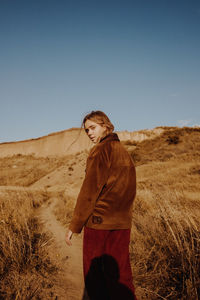 Portrait of woman walking on dirt road against clear sky