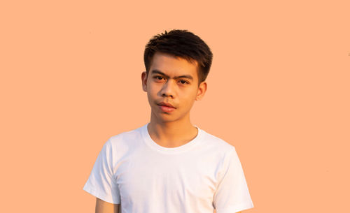 Portrait of young man standing against orange background