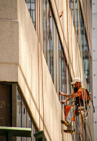 Low angle view of worker washing windows on building