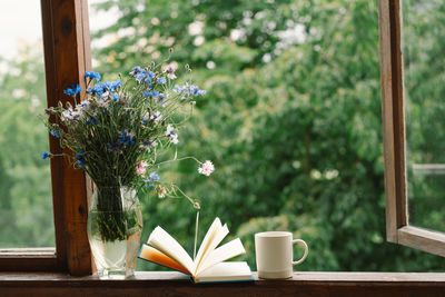 A bouquet of cornflowers and a book on the windowsill in a cozy home.