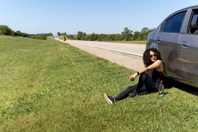 Woman sitting next to her car while relaxing during a road trip.