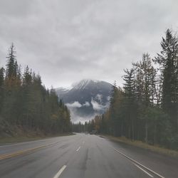 Road amidst trees and mountains against sky