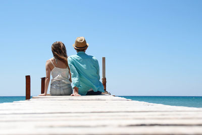 Couple dressed in white and turquoise sitting romantically together in front of the sea