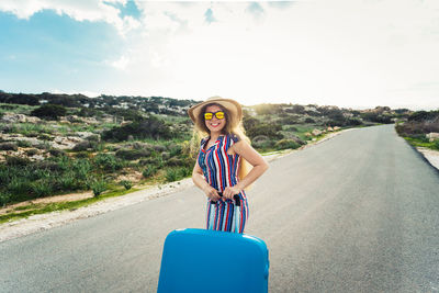 Portrait of young woman standing on road against sky