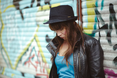 Woman wearing hat against graffiti shutter in city