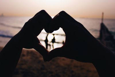 Close-up of hands making heart shape against sea during sunset