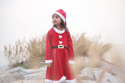Cute girl wearing red dress while standing on rocks against sky during christmas