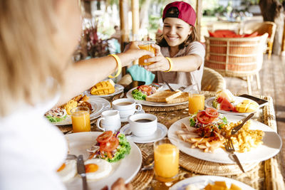 Cropped image of woman giving juice glass to daughter in resort during vacation