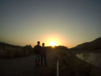 Silhouette men standing on landscape against sky during sunset