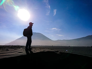 Side view of silhouette man standing on land against sky during sunny day