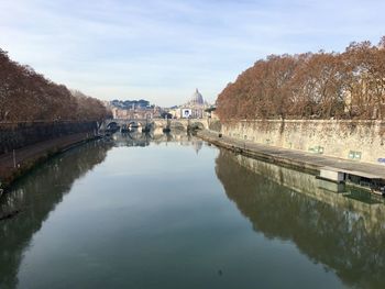 Bridge over river by buildings against sky