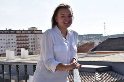 Portrait of smiling young woman standing on roof against buildings in city