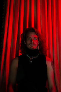 Young man standing by red curtain