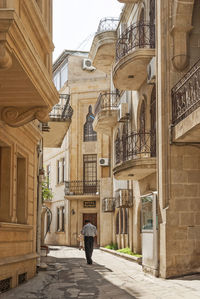 Rear view of man walking on alley amidst buildings in city