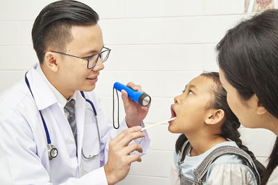 Doctor examining girl sitting by mother at hospital