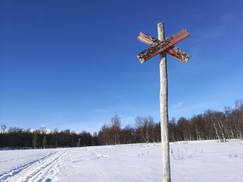 Cross on snow covered land against sky