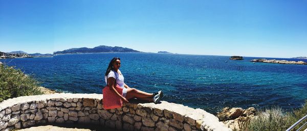 Woman sitting by sea against clear blue sky