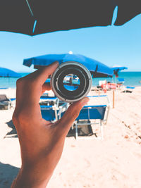 Close-up of hand holding lens at beach against clear sky