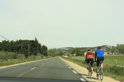 Rear view of man riding bicycle on road against clear sky