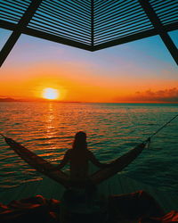 Silhouette woman by sea against sky during sunset