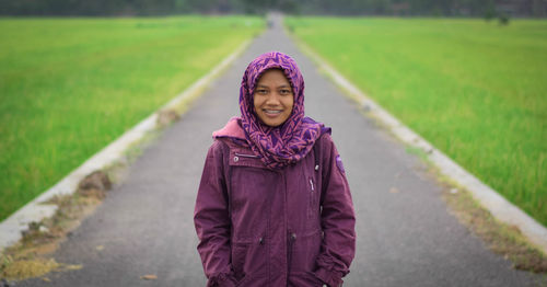 Portrait of smiling woman standing amidst field on road