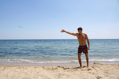 Full length of shirtless man standing at beach against sky