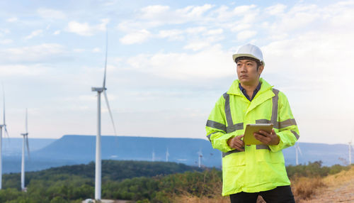 Engineer holding digital tablet standing against sky