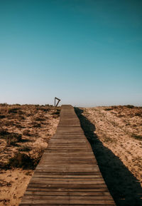 Rear view of man walking on beach against clear blue sky