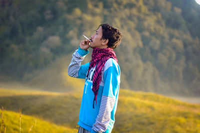 Man smoking cigarette while standing against trees